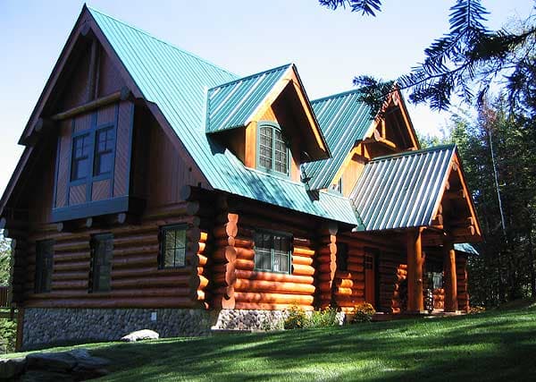 Log home exterior with multiple gables, dormers, stone foundation, and metal roof.