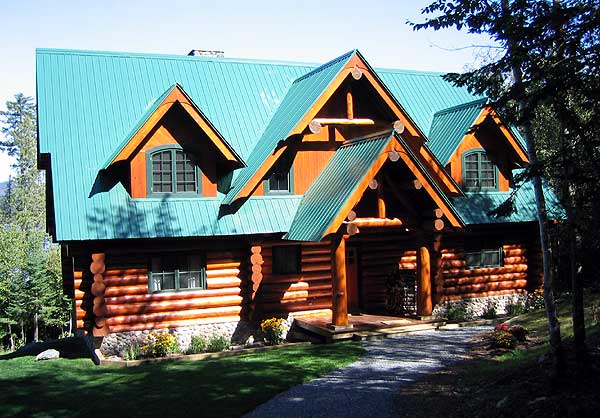 Log cabin house plan exterior with green metal roof, prominent gables, and stone foundation. Features exposed log construction.
