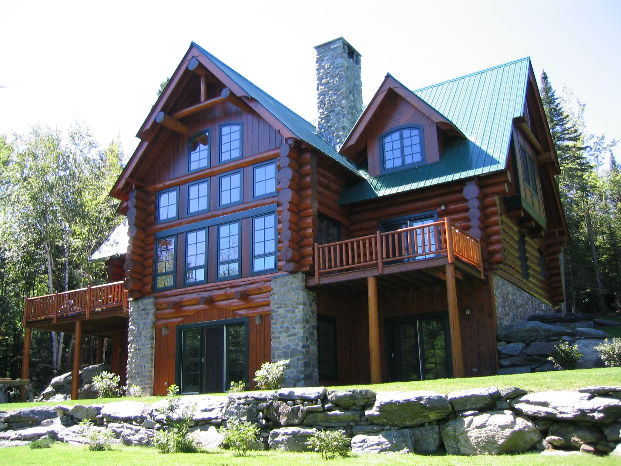 Log home exterior with multiple stories, stone foundation, and upper-level balcony.