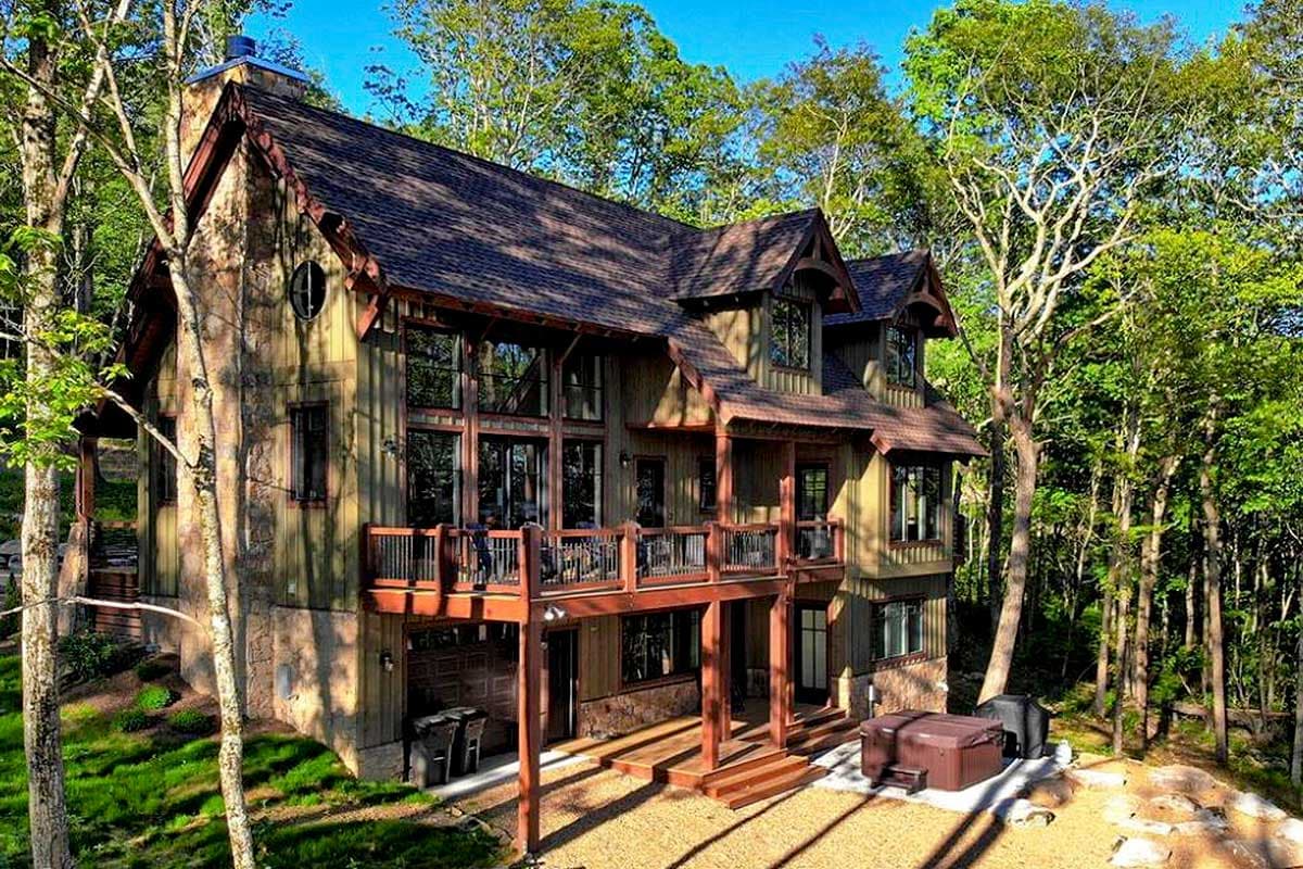 House plan exterior: Two-story mountain lodge style with stone chimney, large windows, and wraparound deck.