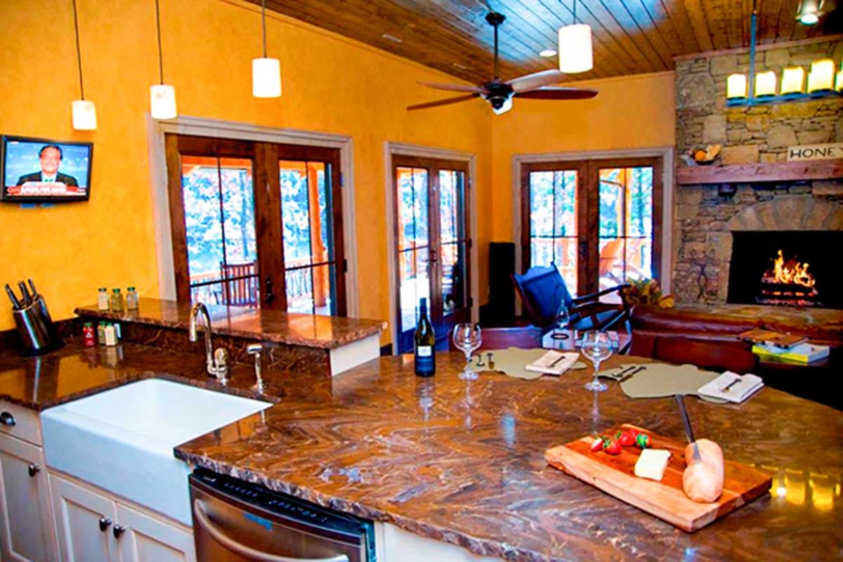 Kitchen island with sink, wood-paneled ceiling, stone fireplace, and double doors leading outdoors.