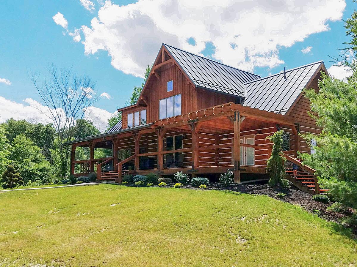 Log cabin house plan exterior with a wraparound porch, gabled dormers, and a metal roof.