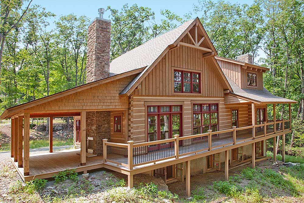 Log cabin house plan exterior with stone chimney, covered porch, and deck. Two stories with prominent gables and wood siding.