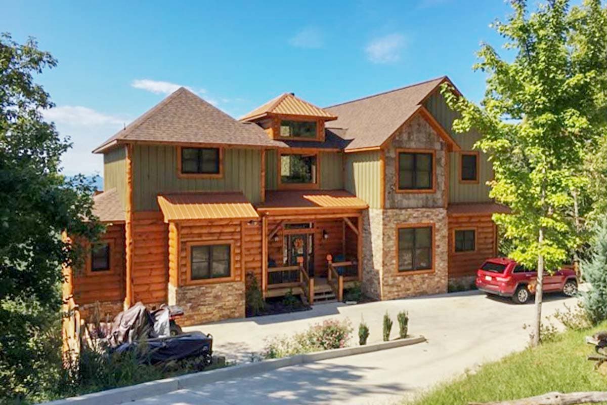 House plan exterior. Two-story rustic home with log siding and stone accents. Features include a front porch, gables, and metal roof accents.