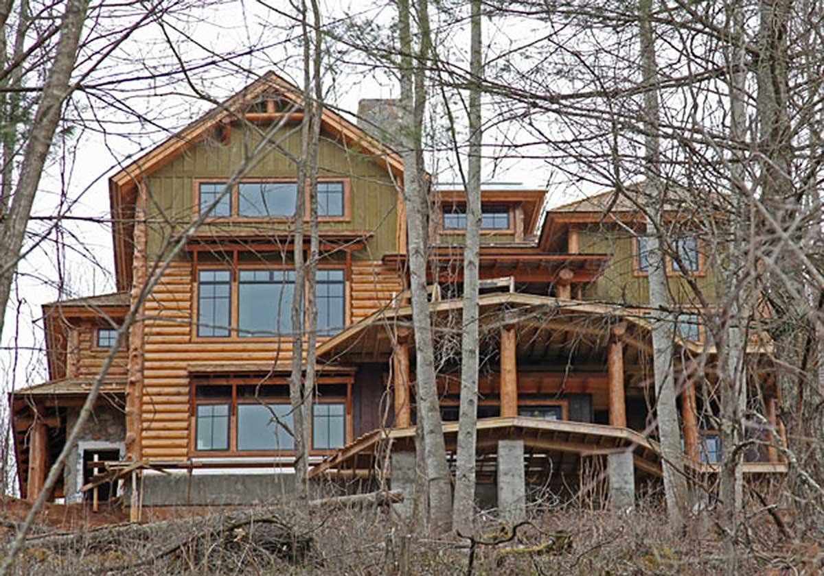 House plan exterior for a multi-story log home with gables, multiple porches supported by log posts, and stacked dormers.