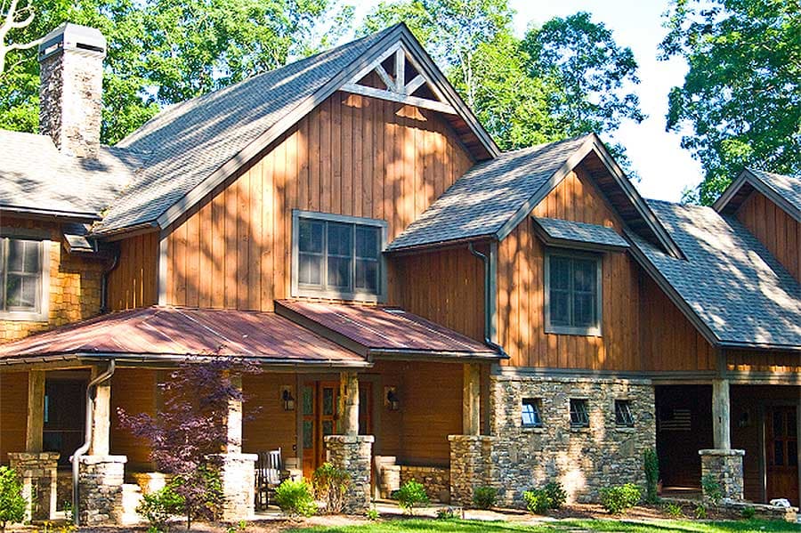 House plan exterior with timber siding, stone foundation, metal roof, prominent stone chimney, and covered porch.