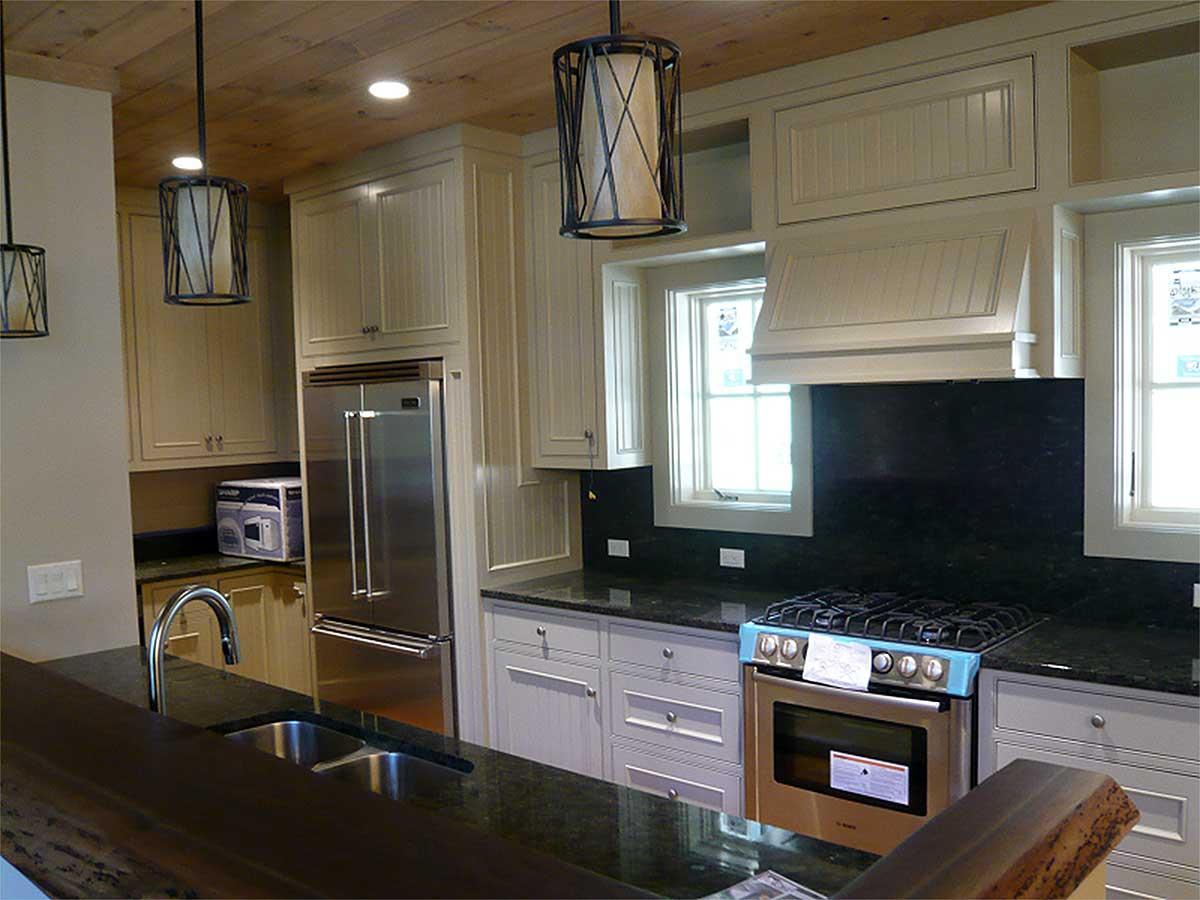 Kitchen with stainless steel refrigerator, dual basin sink, granite countertops, and a gas range with a custom hood.