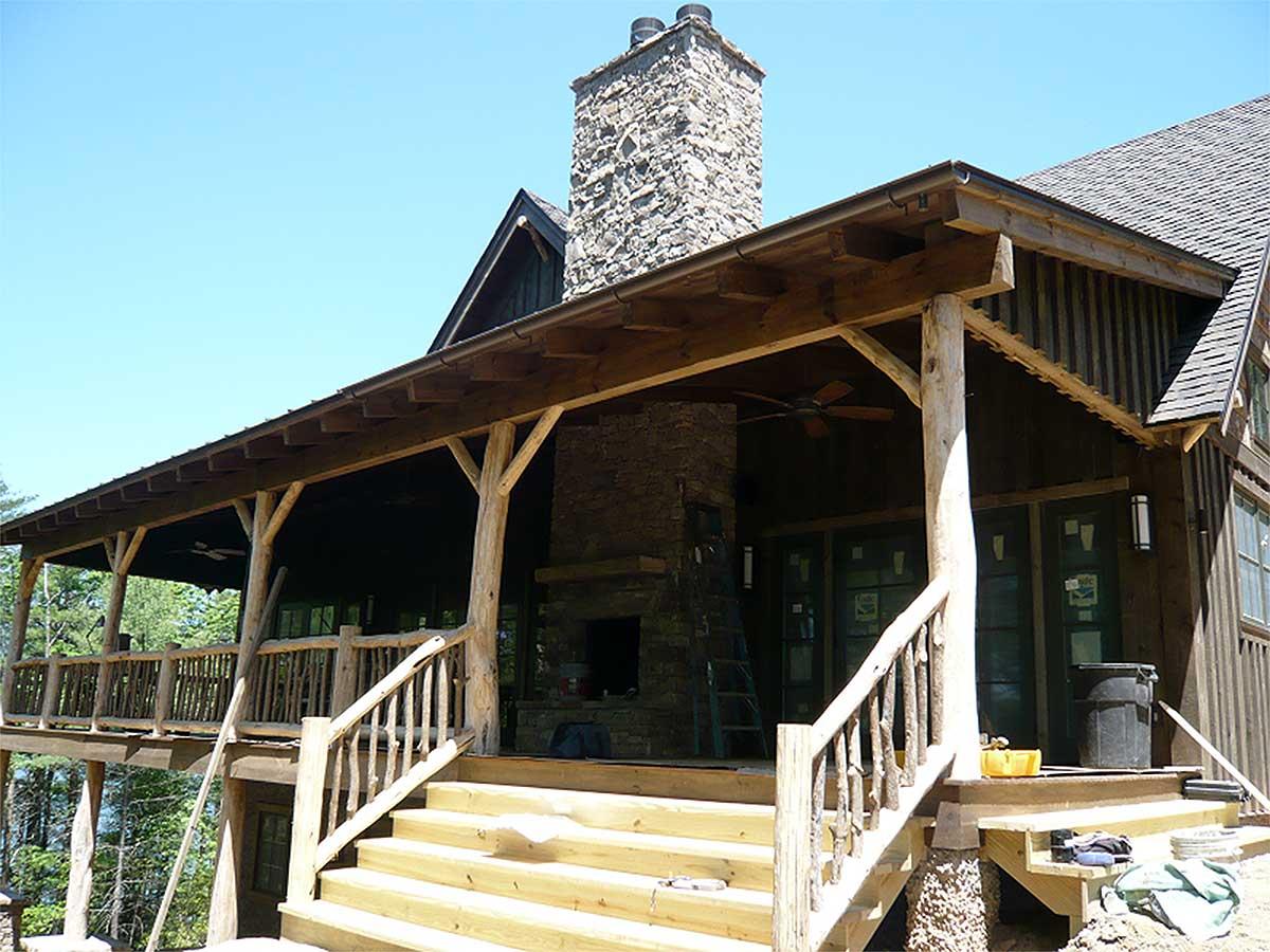 House plan exterior with a large covered porch, stone chimney, and wood siding.