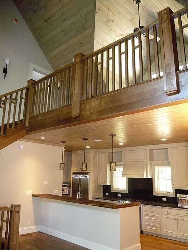 Interior view of a kitchen with a breakfast bar, stainless steel refrigerator, white cabinetry, and a wooden loft railing above.