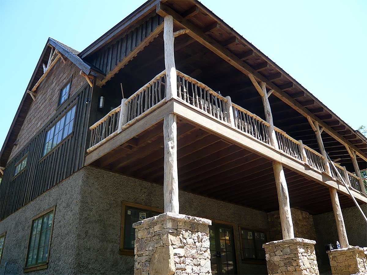 House plan exterior featuring a multi-story design with stone foundation, rustic wood siding, and a wrap-around porch with log railings.