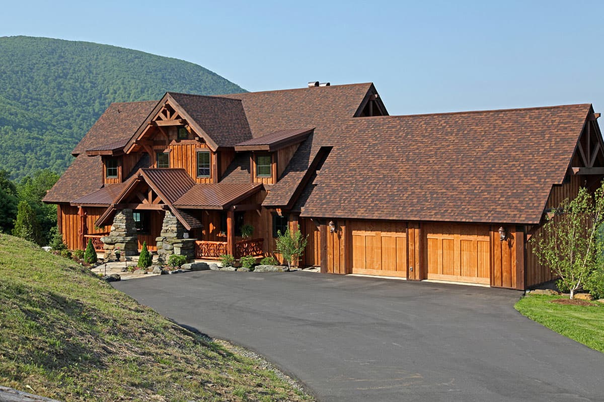 Log cabin house plan exterior with a multi-gabled roof, stone foundation, covered porch, and a three-car garage.