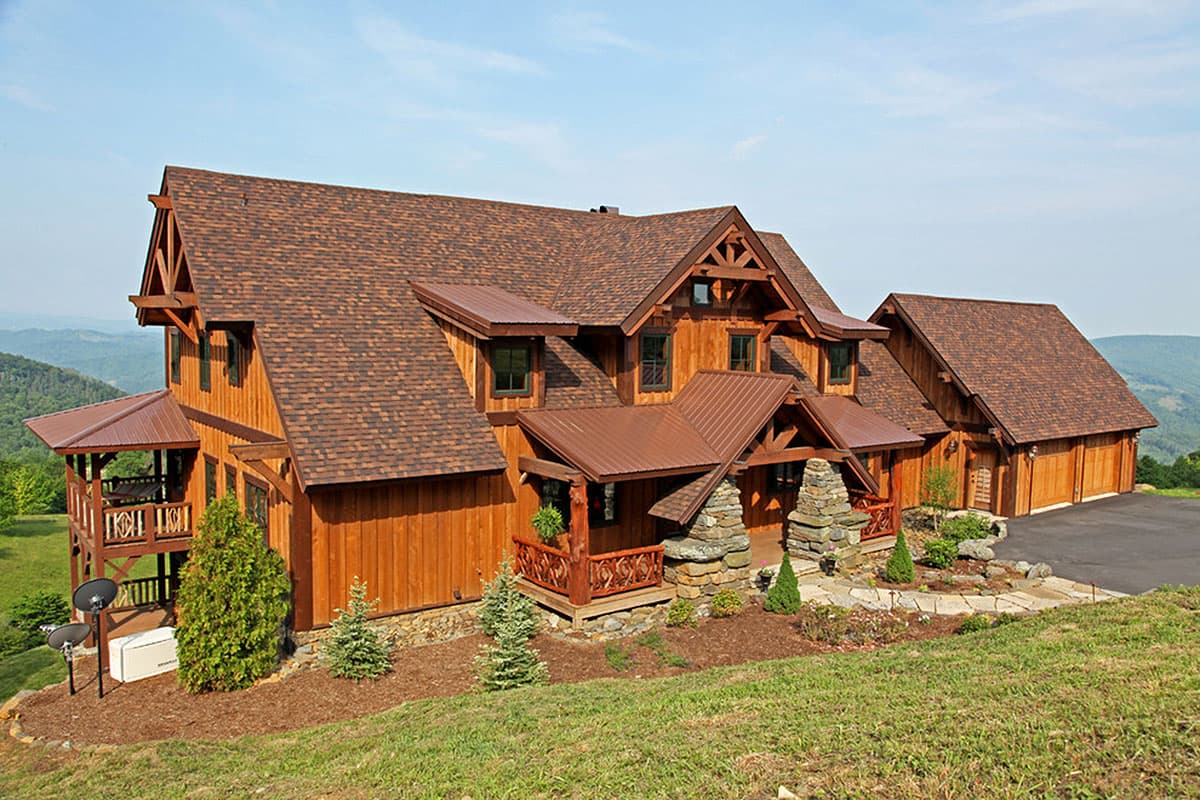 Log home exterior with wood siding, steeply pitched gables, dormers, stone accents, and a detached three-car garage.