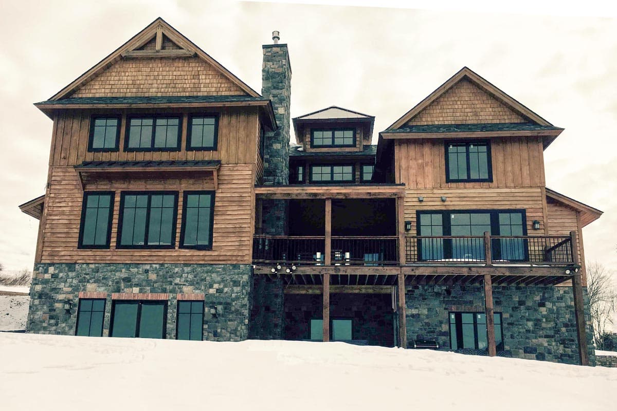 House plan exterior featuring stacked stone base, wood siding, multiple gables, stone chimney, and balconies.