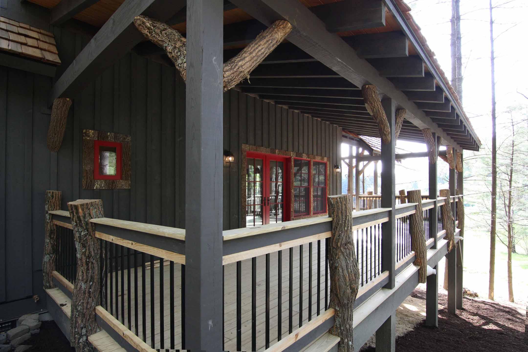 House plan exterior with dark siding, a covered porch with log supports, and red-trimmed windows and doors.