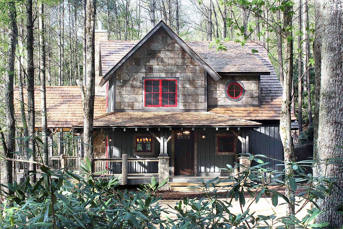 House plan exterior: Two-story rustic home with cedar shake siding, a deep porch, and red-framed windows.