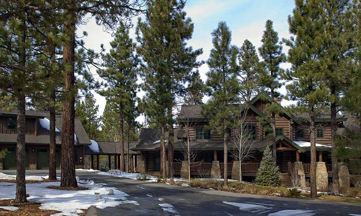 Log cabin exterior with a covered porch, stone accents, multiple gables, and attached garage.