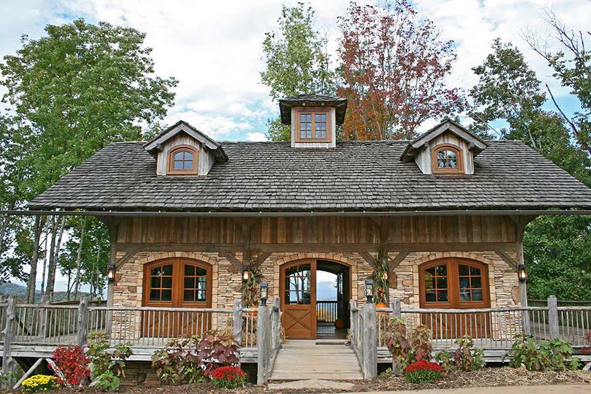 House plan exterior featuring stone and wood facade, arched windows, wood shake roof, and dormer windows.