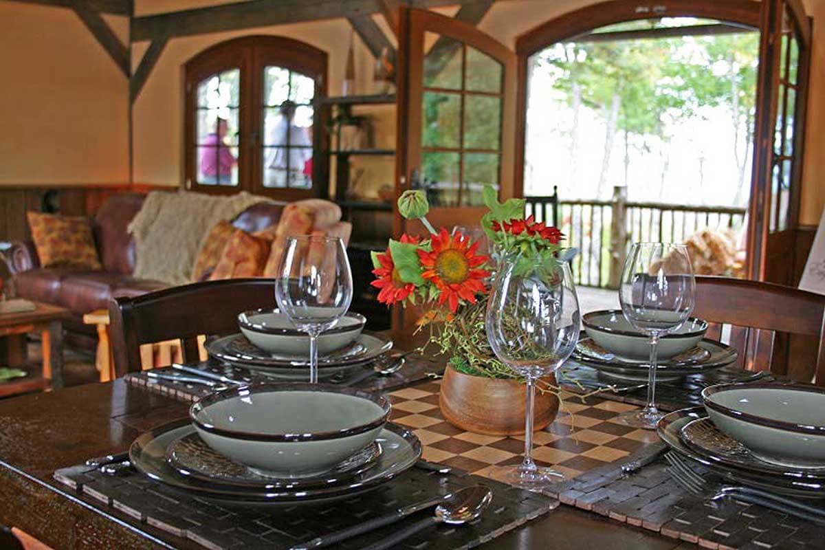 Dining area with a table set for dinner, visible wooden beams, arched doorways, and French doors leading to an outdoor deck.
