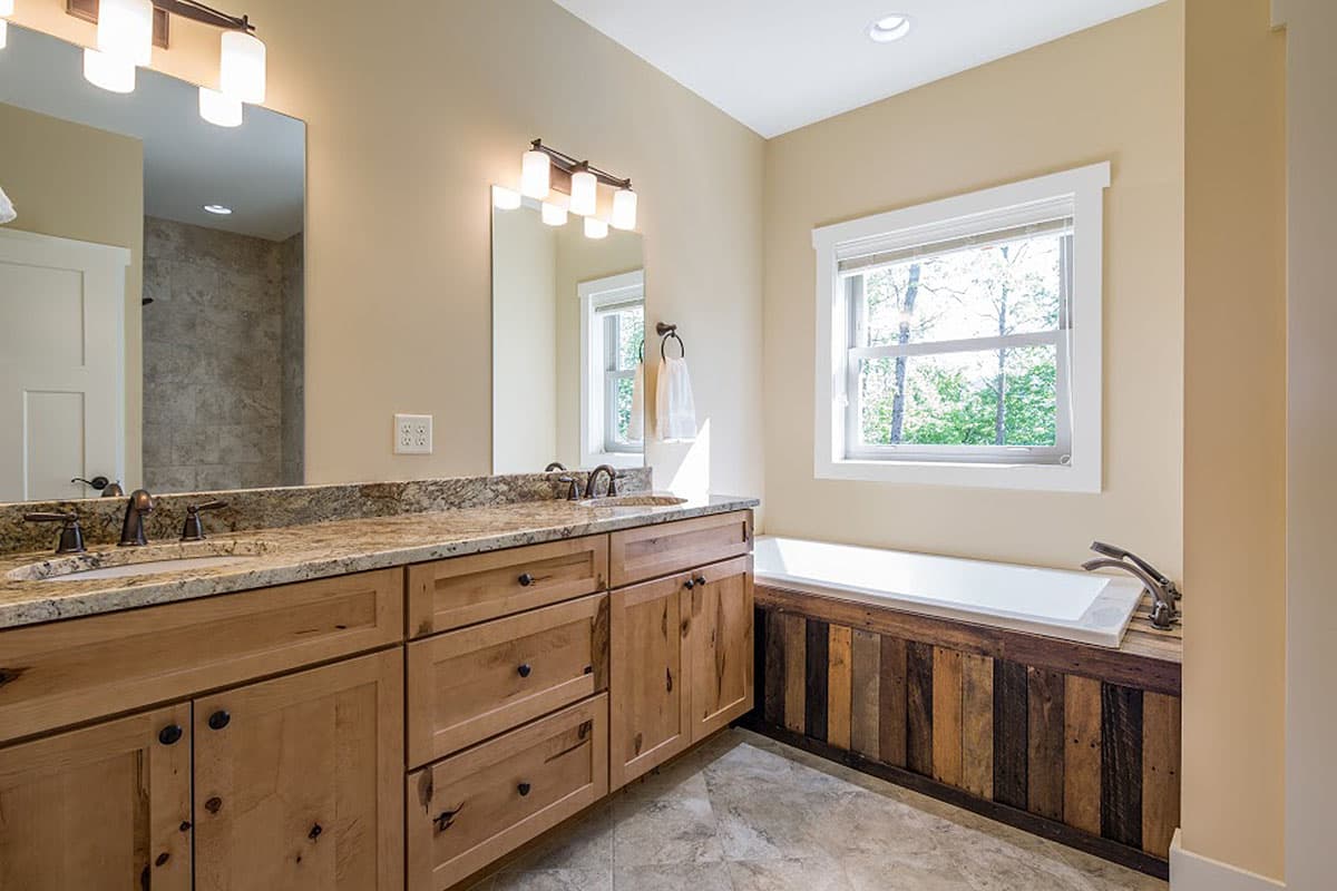 Bathroom with double vanity, granite countertops, wood cabinetry, and a soaking tub with a wood-paneled skirt.