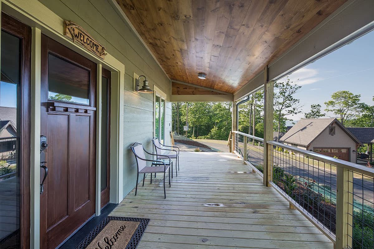 House plan exterior: Covered porch with wood ceiling, railing, and seating. Features a dark wood front door.