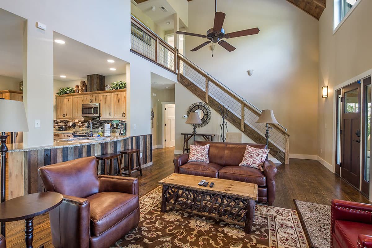 Open-concept living space with vaulted ceiling, kitchen with island, and staircase with metal railing.