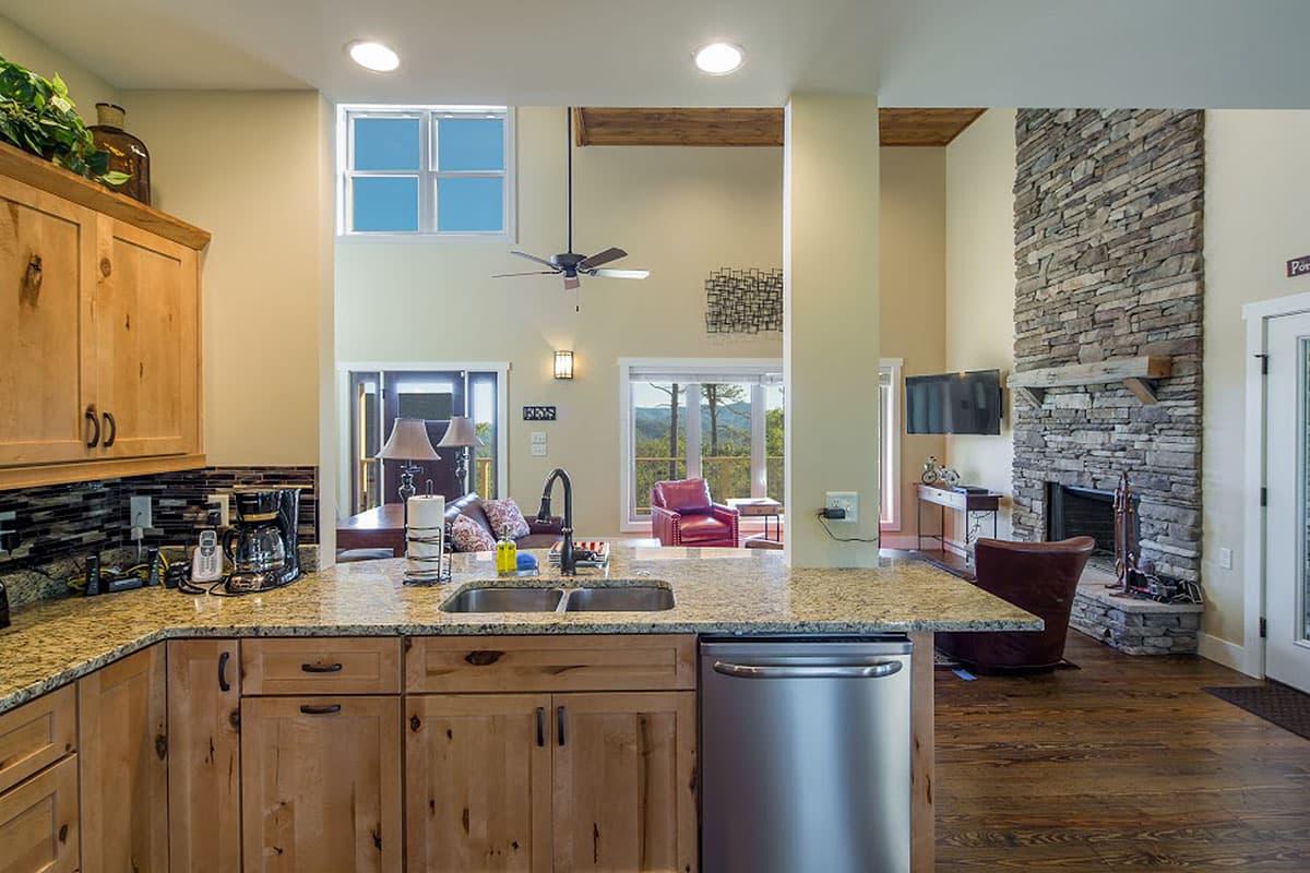 Open concept living area featuring a kitchen island, stone fireplace, and vaulted ceilings with exposed beams.