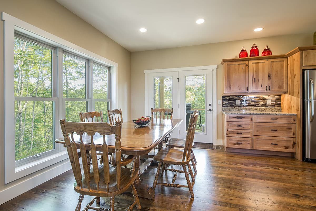 Dining area with wooden table and chairs, large windows, and wood cabinetry with granite countertops.