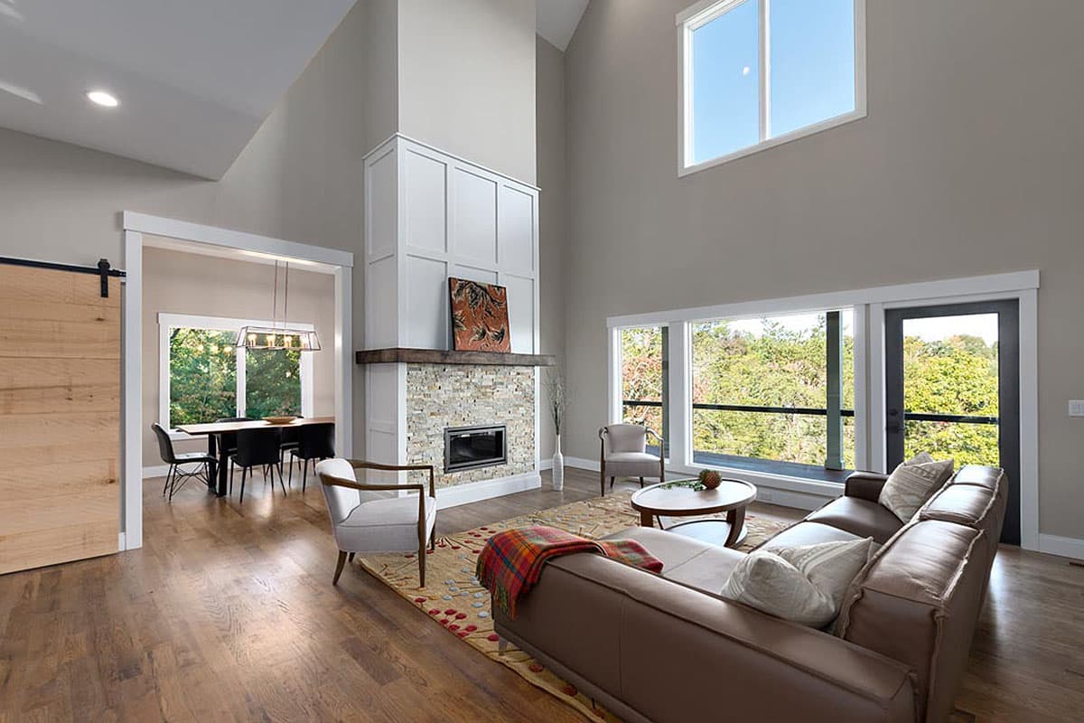 Great room with vaulted ceiling, stone fireplace, large windows, and adjacent dining area with sliding barn door.
