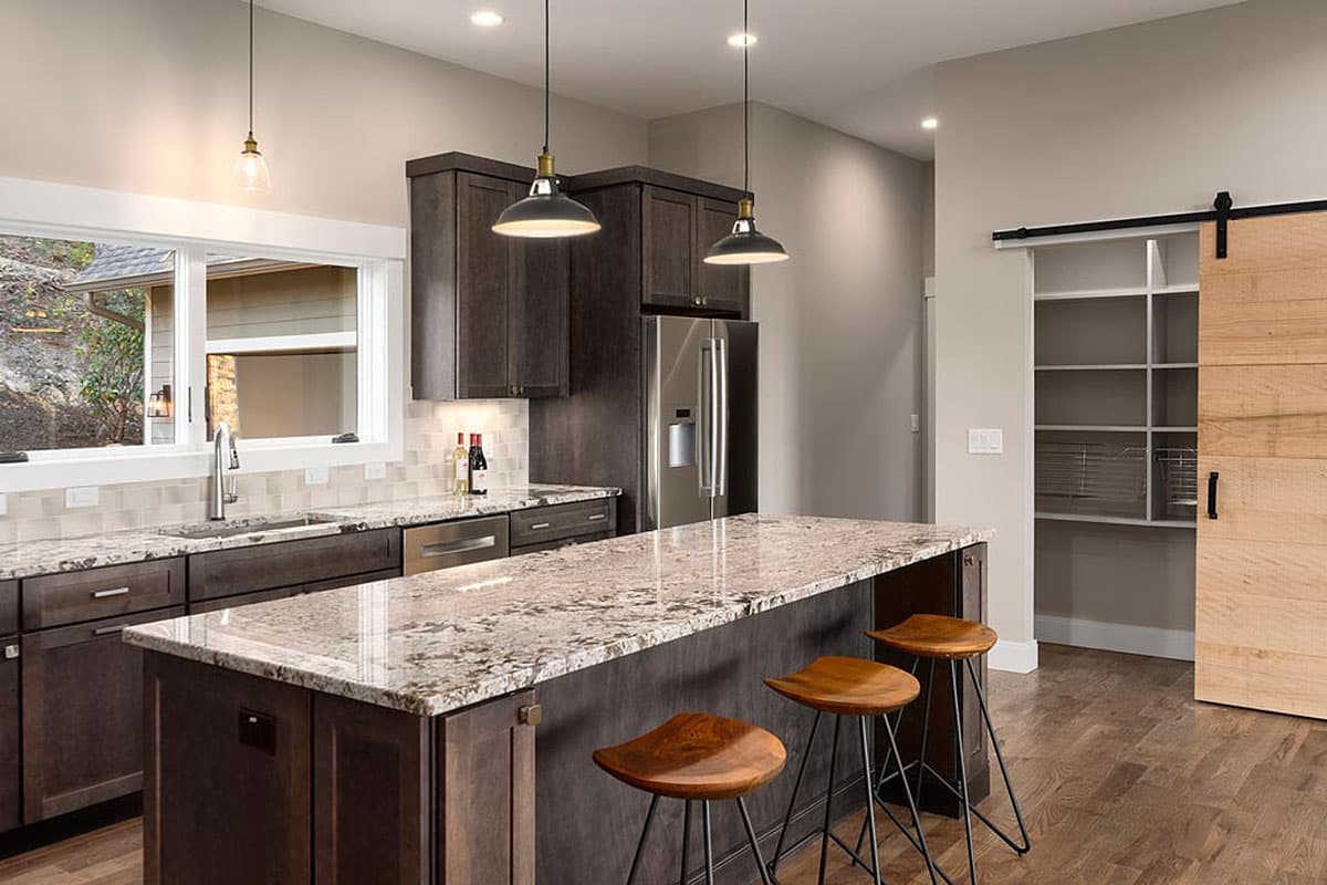 Kitchen featuring dark wood cabinets, granite countertops, island with bar stools, and a sliding barn door pantry.