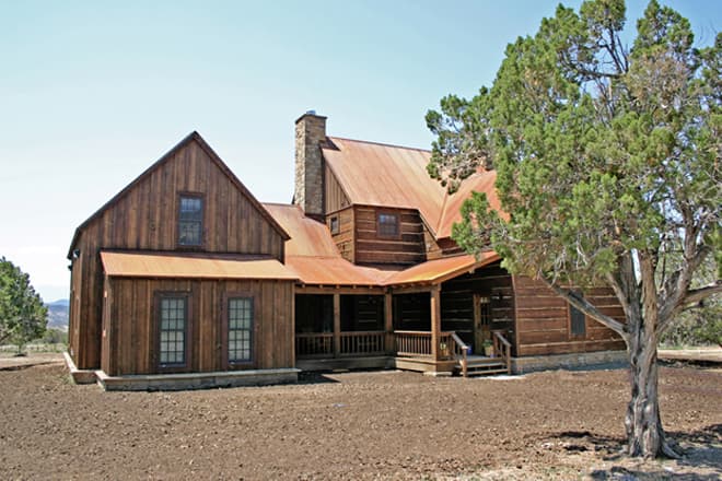 House plan exterior of a two-story log home with a metal roof, stone chimney, and wraparound porch.