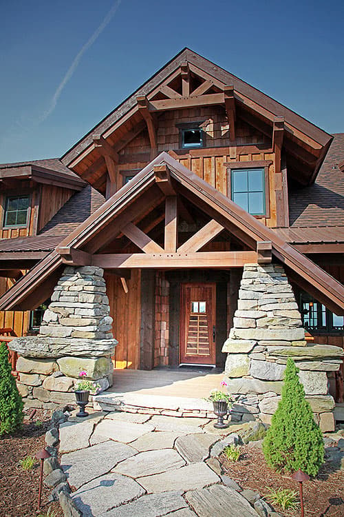 House plan exterior with heavy timber framing, stone pillars, and a covered entryway with a wood-paneled door.