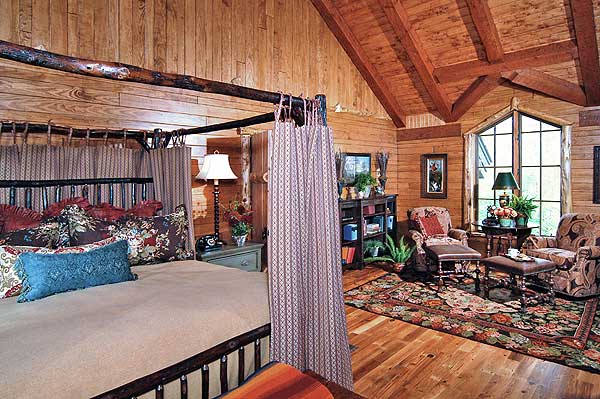 Interior view of bedroom with wood-paneled walls and ceiling, four-poster bed, sitting area with chairs and ottoman, and a large window.
