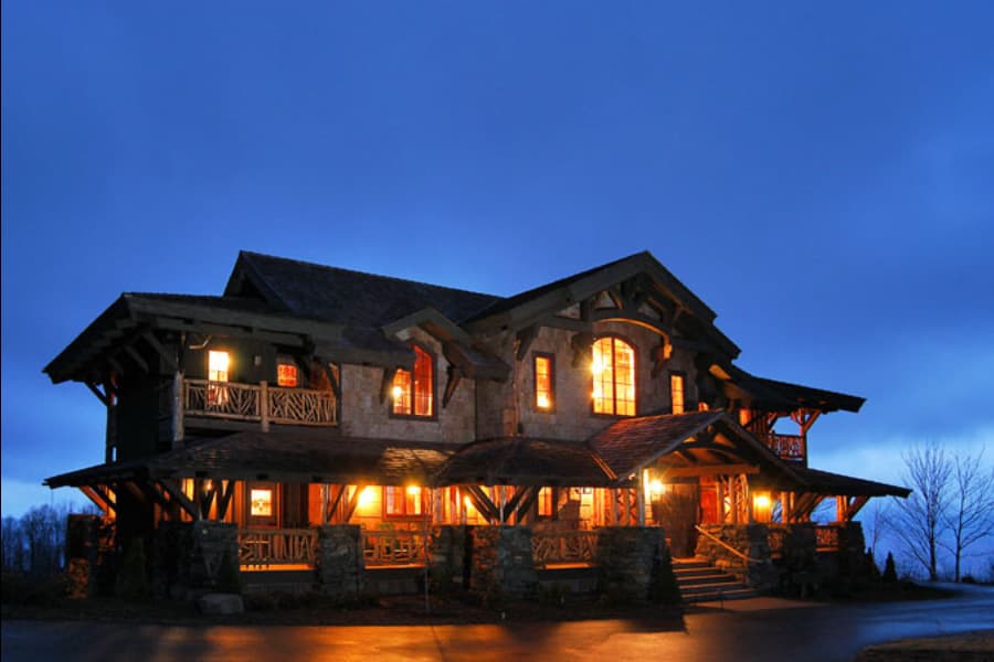 Rustic lodge-style house plan exterior with prominent timber framing, stone accents, multiple gables, and covered porches.