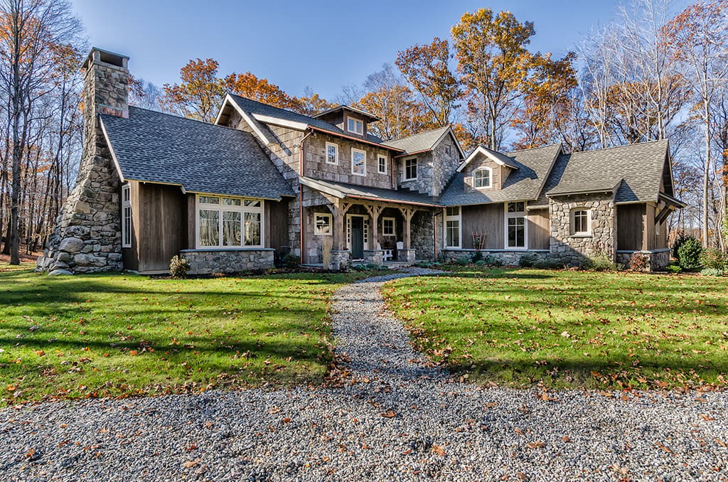House plan exterior: Stone and wood siding, prominent stone chimney, covered porch with timber supports, multiple gables.