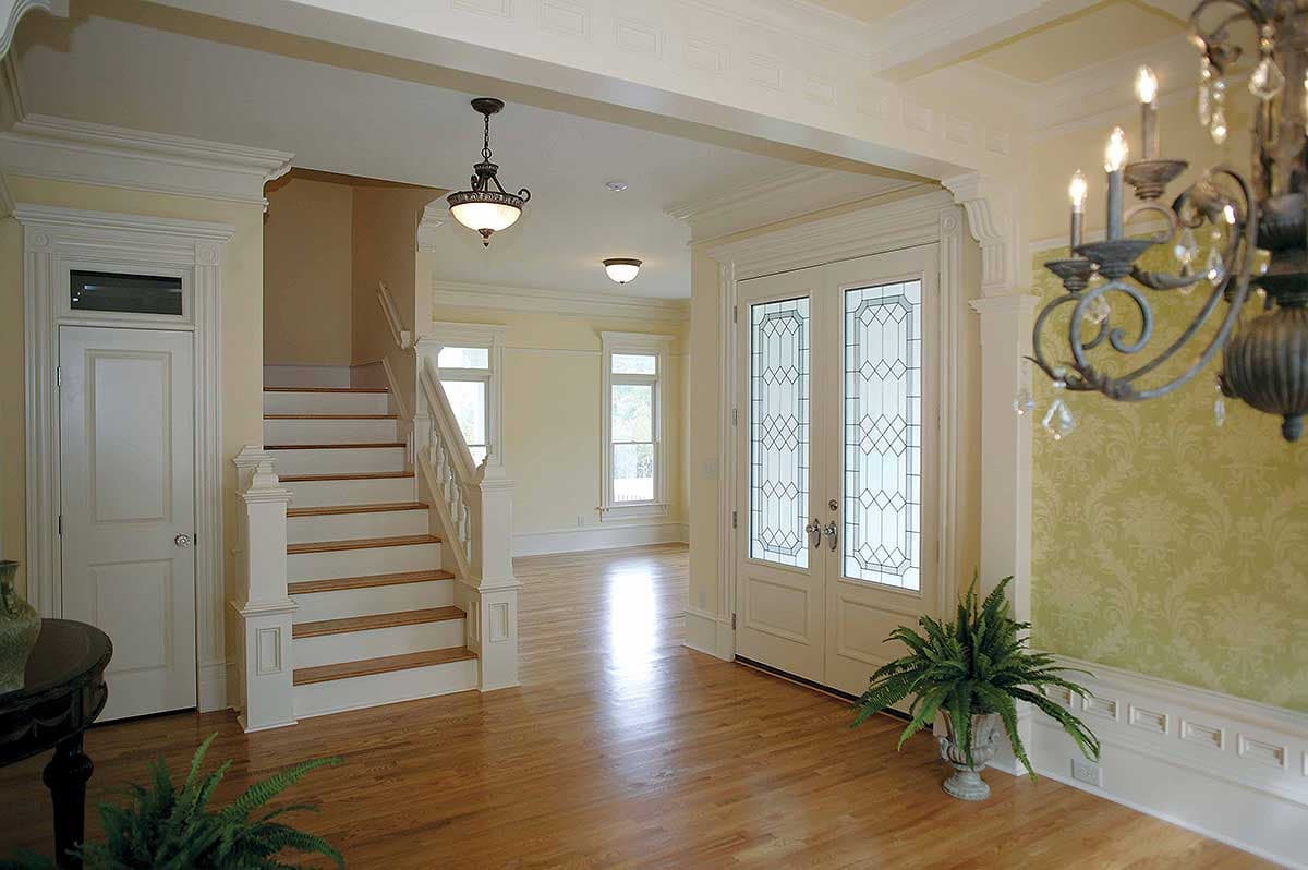 Interior view: Entry hall with double doors featuring stained glass, a staircase, and decorative molding.