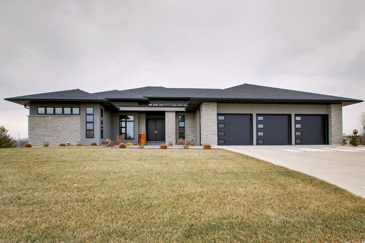 House plan exterior. Modern style, single story home with flat roof, recessed entry, and three-car garage. Stone and stucco exterior.