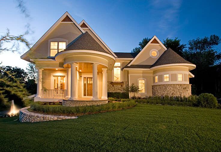 House plan exterior with rounded columned porch, stone foundation, multiple gables, and a turret.