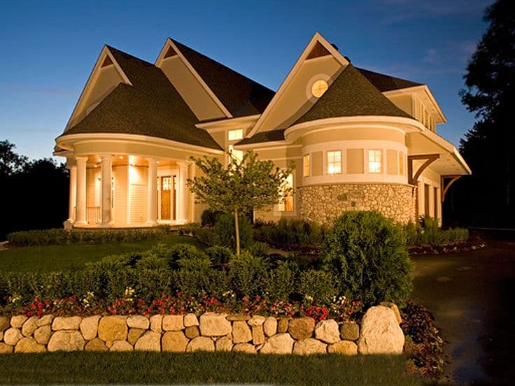 House plan exterior with a curved porch, columns, stone accents, gables, and a turret.