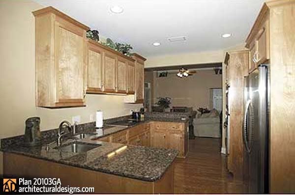 Kitchen with wood cabinets, granite countertops, and stainless steel refrigerator, opening to a living area.