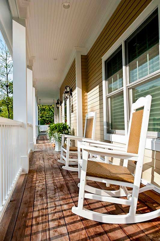 House plan exterior: wraparound porch with white balustrade, columns, beadboard ceiling, and rocking chairs.