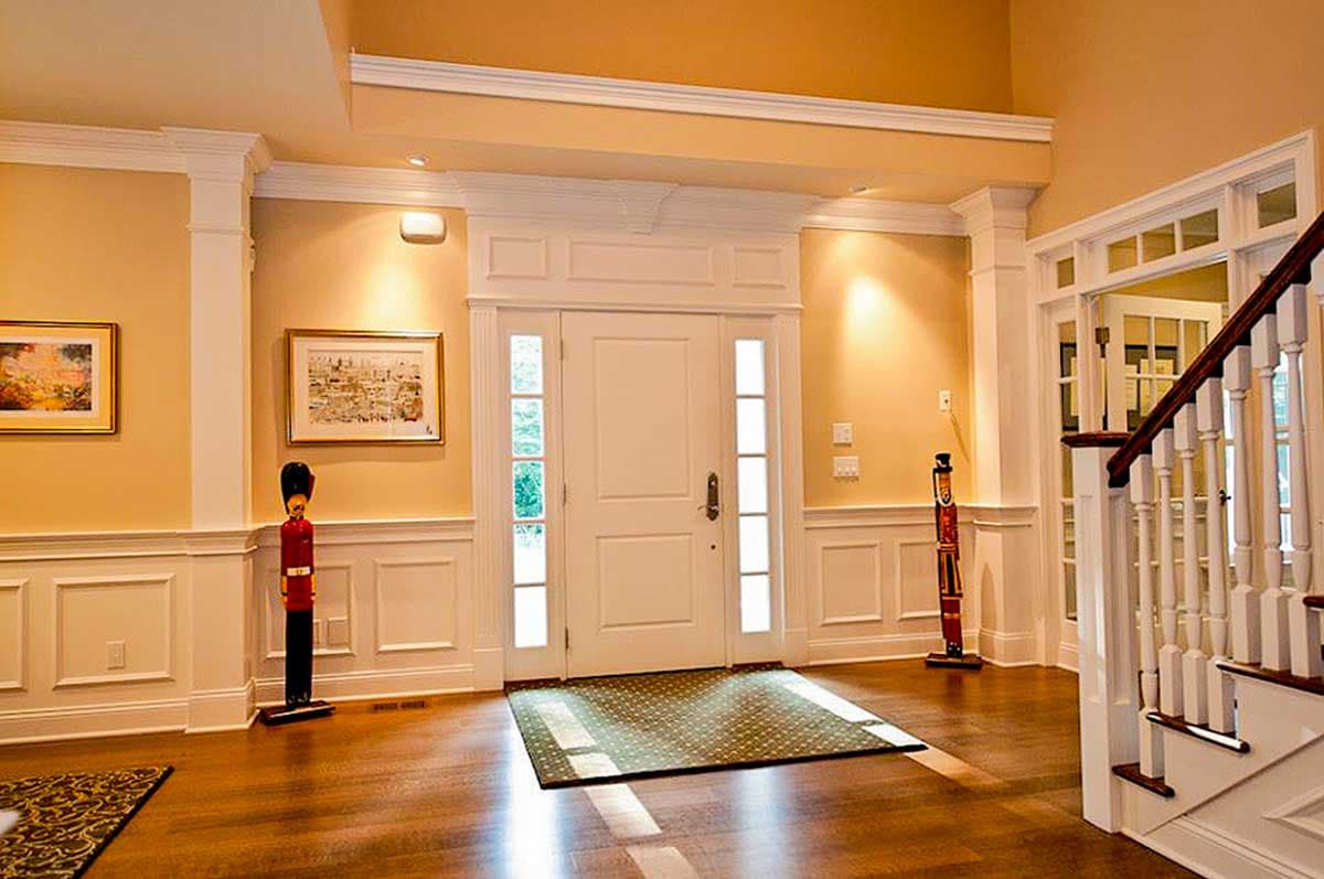 Interior view of a house entryway with a white double door, sidelights, wainscoting, and a staircase.