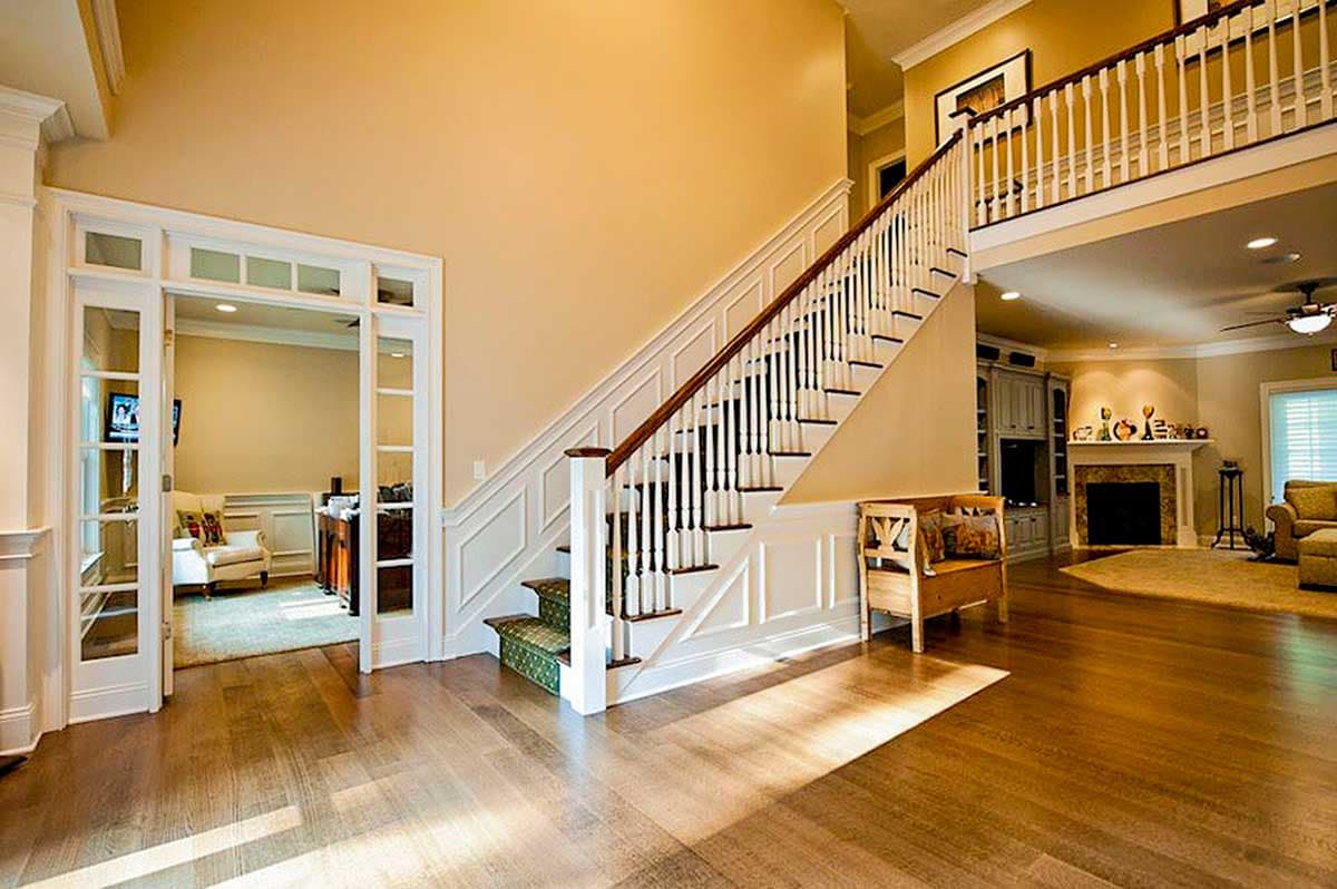 Interior view of a two-story house foyer with a grand staircase, wainscoting, and double doors leading to a study.