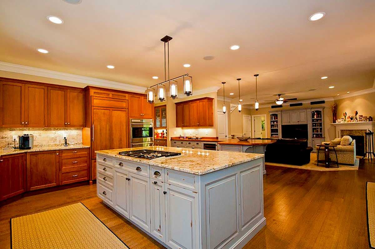 Kitchen with light blue island, granite countertops, and wood cabinetry. Adjacent open living area with fireplace.