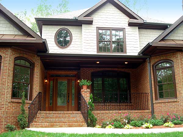 House plan exterior: brick and shingle siding, covered porch with arched windows, dual gables, and a rounded dormer window.