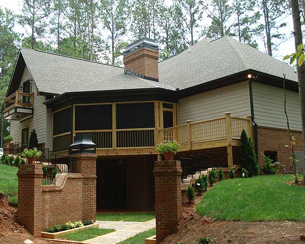 House plan exterior showing a multi-level house with a screened porch, wooden deck, brick accents, and a prominent chimney.