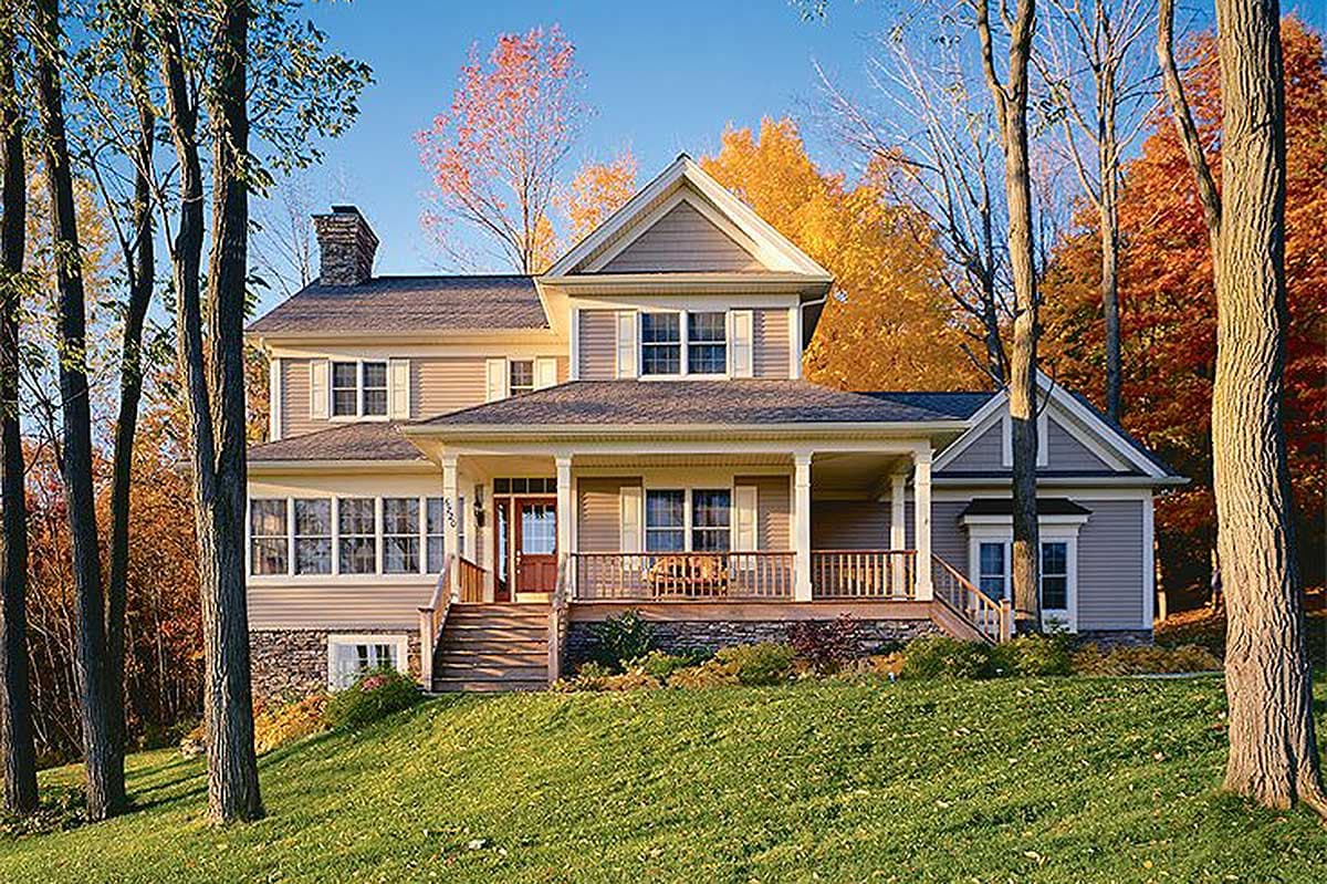 Two-story house plan exterior with wraparound porch, stone foundation, gable dormers, and large gabled entrance.