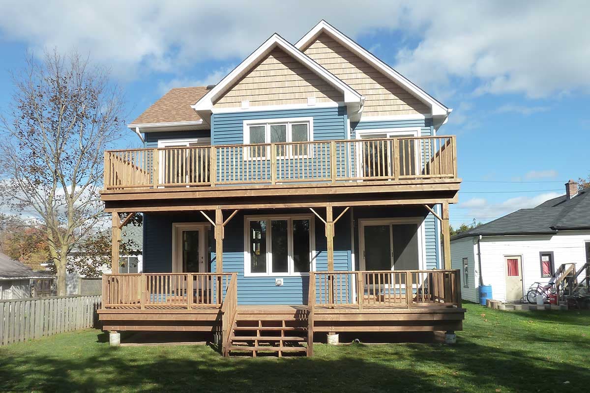 House plan exterior: two-story blue house with cedar shingle gables and two expansive wooden decks.