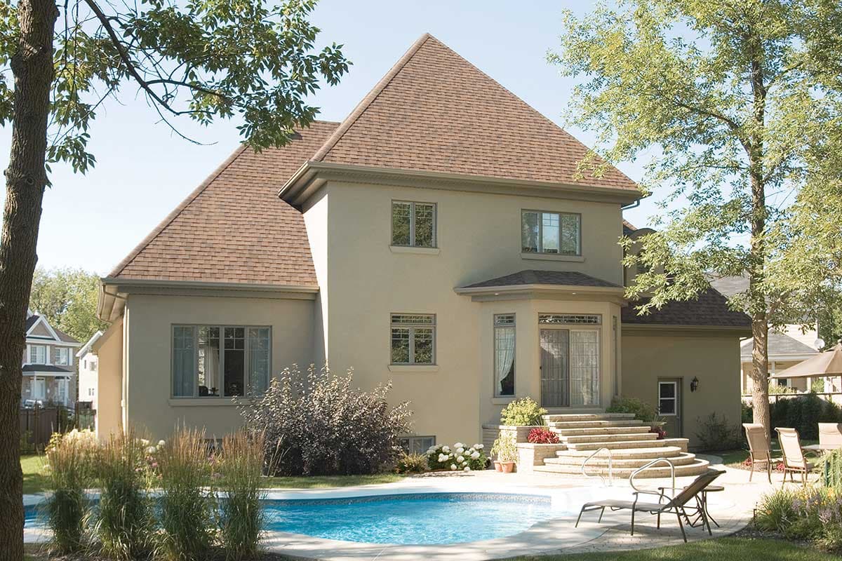 House plan exterior: Two-story stucco home with multi-level roof, central bay window, and stone steps to patio.