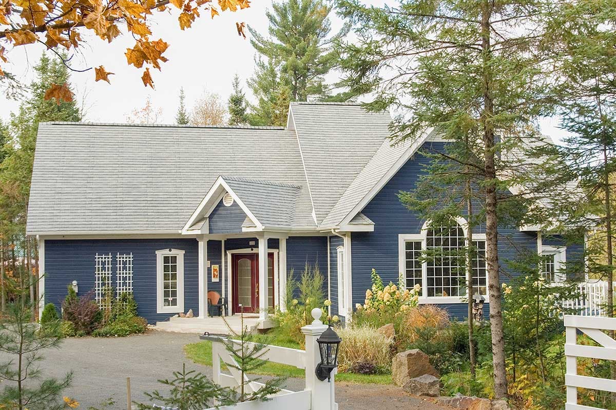 House plan exterior. Two-story home with a gabled roof, dormers, and a front porch. Features include large windows and dark blue siding.