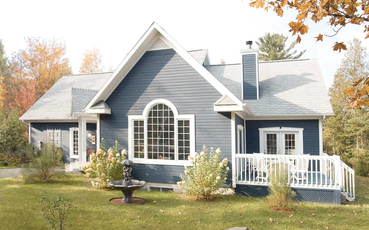 House plan exterior: Dark blue siding, gabled roof, arched window, and white-railed deck.
